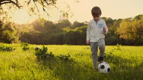 Junge-Steht-Im-Sommer-Mit-Einem-Fußball-Bei-Sonnenuntergang-Und-Schaut-In-Die-Kamera.